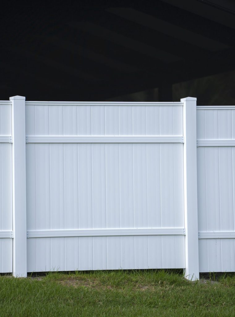 White vinyl picket fence on green lawn surrounding property grounds for backyard protection and privacy.